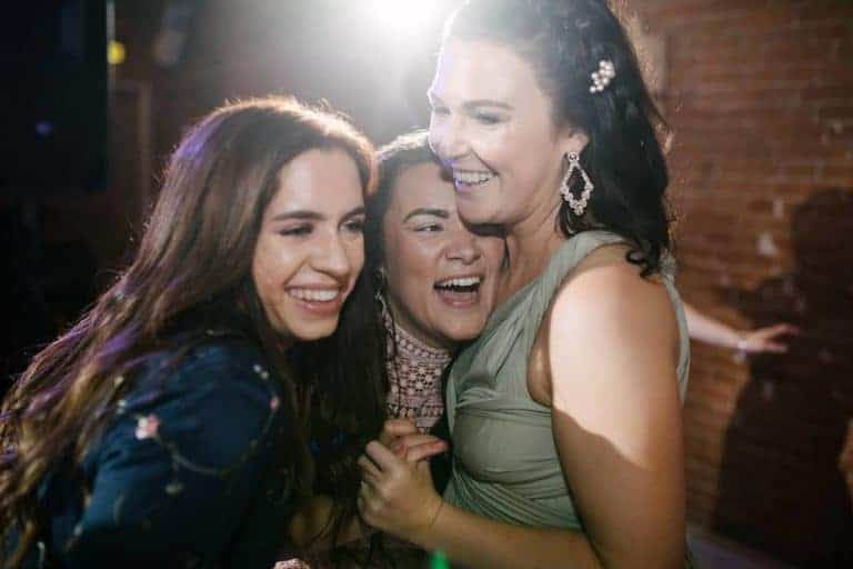 Friends hugging and laughing on the dance floor at an Elsham Hall wedding