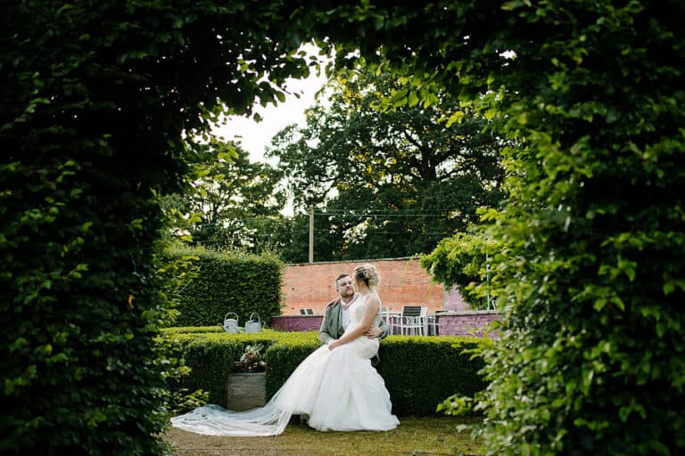 Bride framed by a green garden archway at Elsham Hall, North Lincolnshire