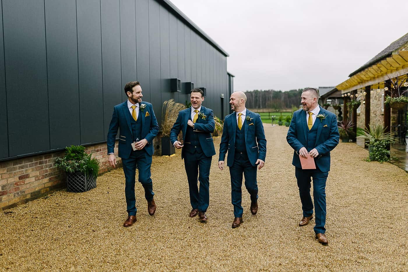 groom and groomsmen walking on the gravel outside of Bunny Hill weddings next to the black clad wedding barn