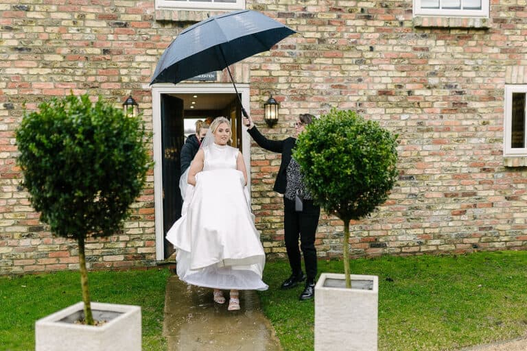 Bride holding her dress under an umbrella on a rainy winter wedding day at Bunny Hill, East Yorkshire