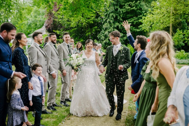 Bride and groom laughing as guests throw confetti in the gardens at Elsham Hall