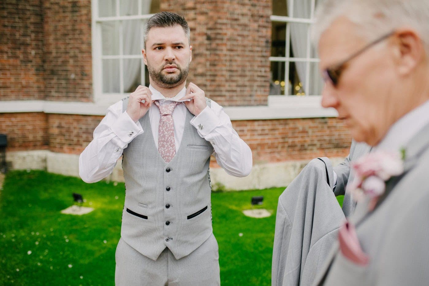 Groom Harry fastening his collar out in the gardens while getting ready on the morning of his wedding