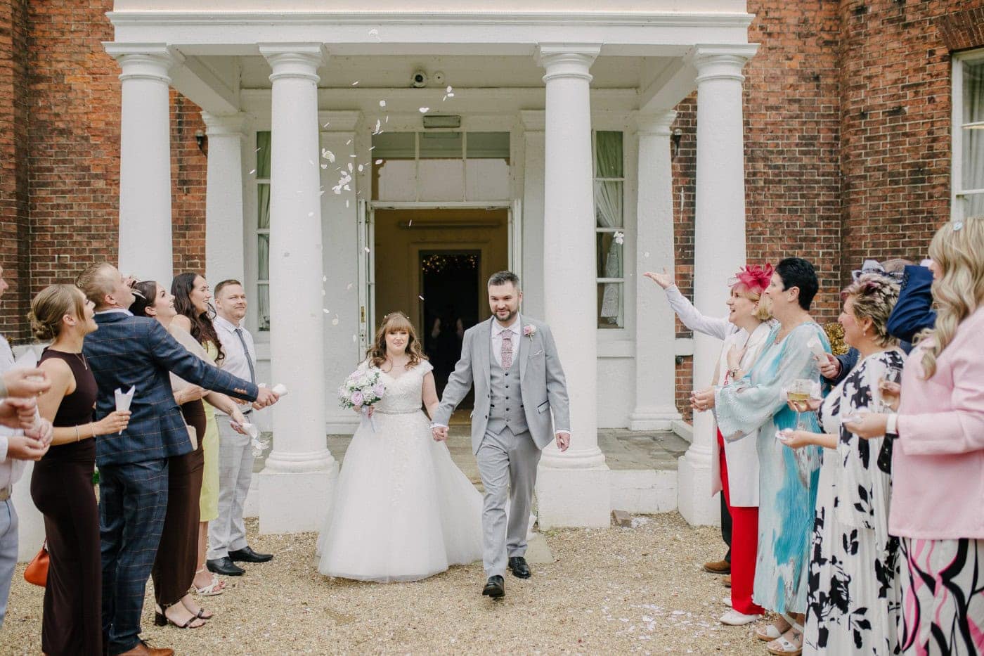 Guests throwing confetti over the bride and groom outside the white columned porch at Bawtry Hall