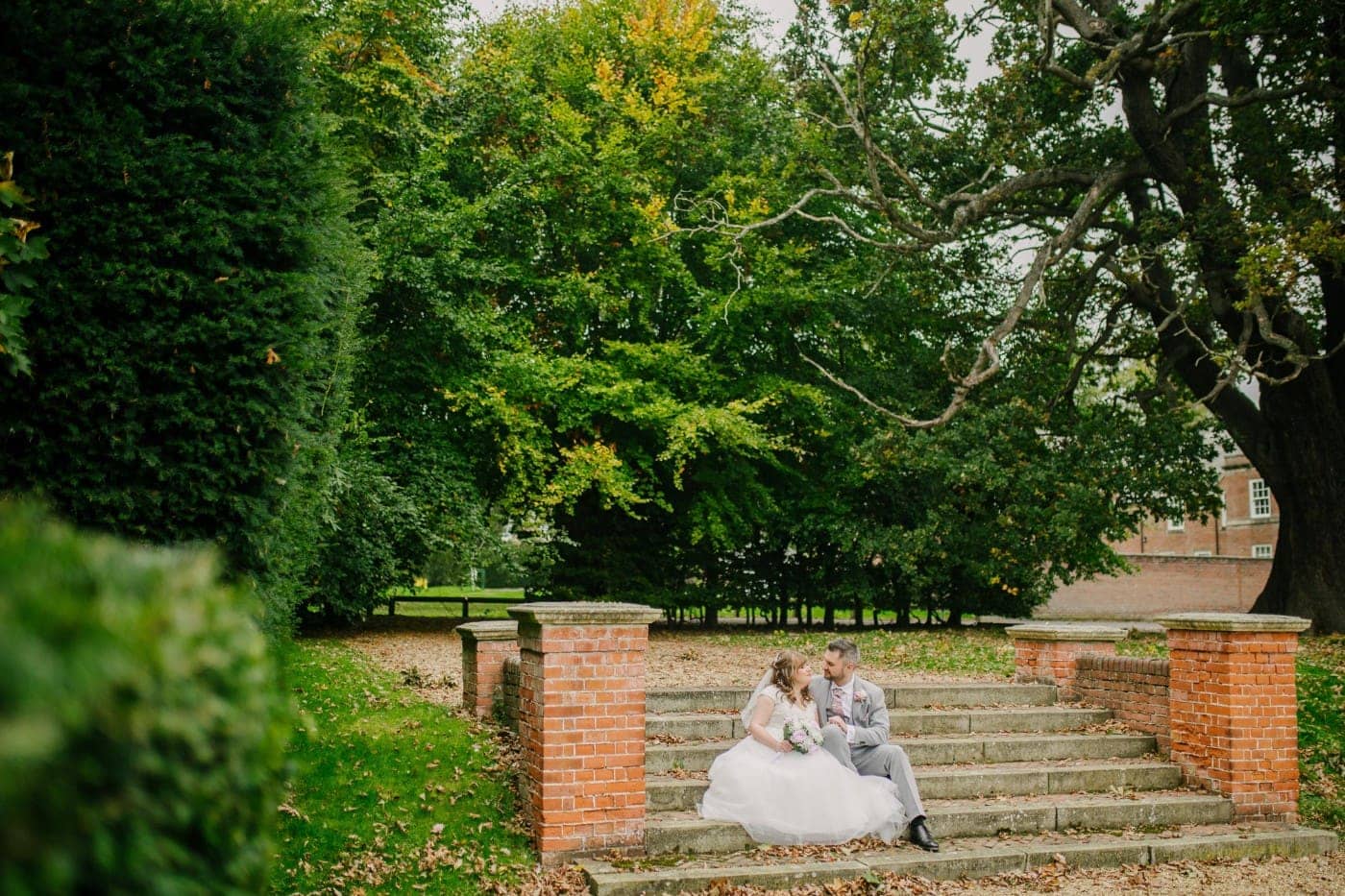 The couple sitting together on the garden steps among the trees, chatting and laughing in soft natural light