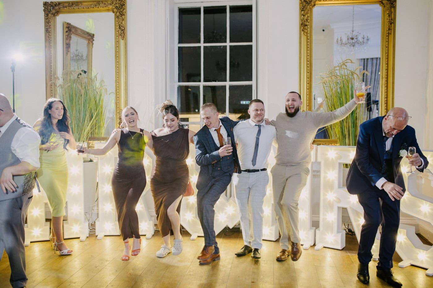 Guests dancing in a line in front of the glowing letters