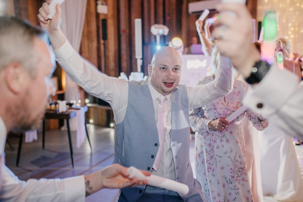 Groomsman cheering with his arms in the air on the packed dance floor