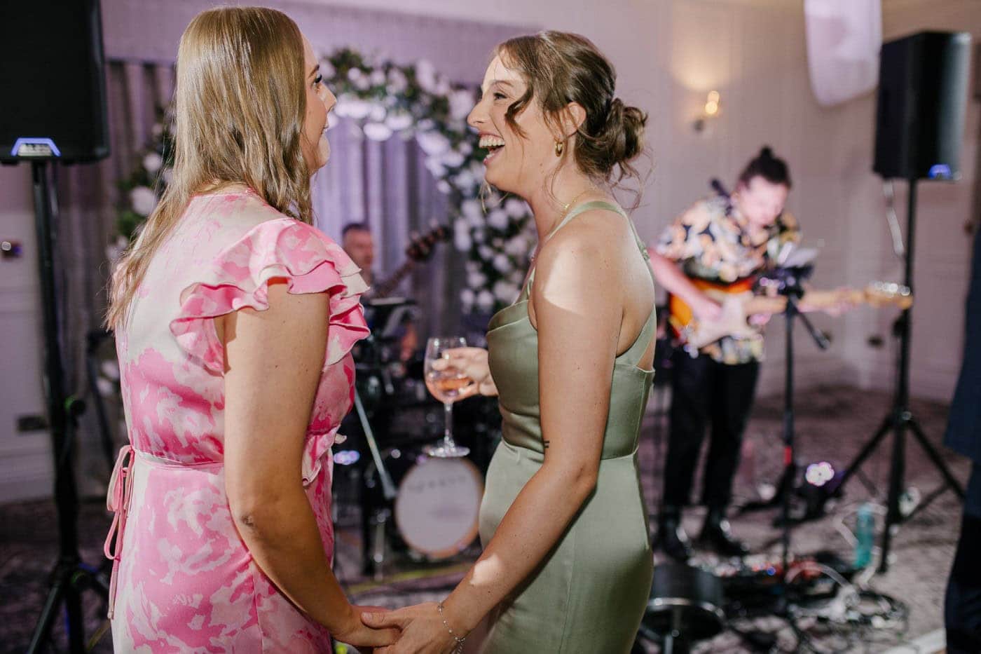 Bridesmaids in sage green dancing together on the packed dance floor in the evening