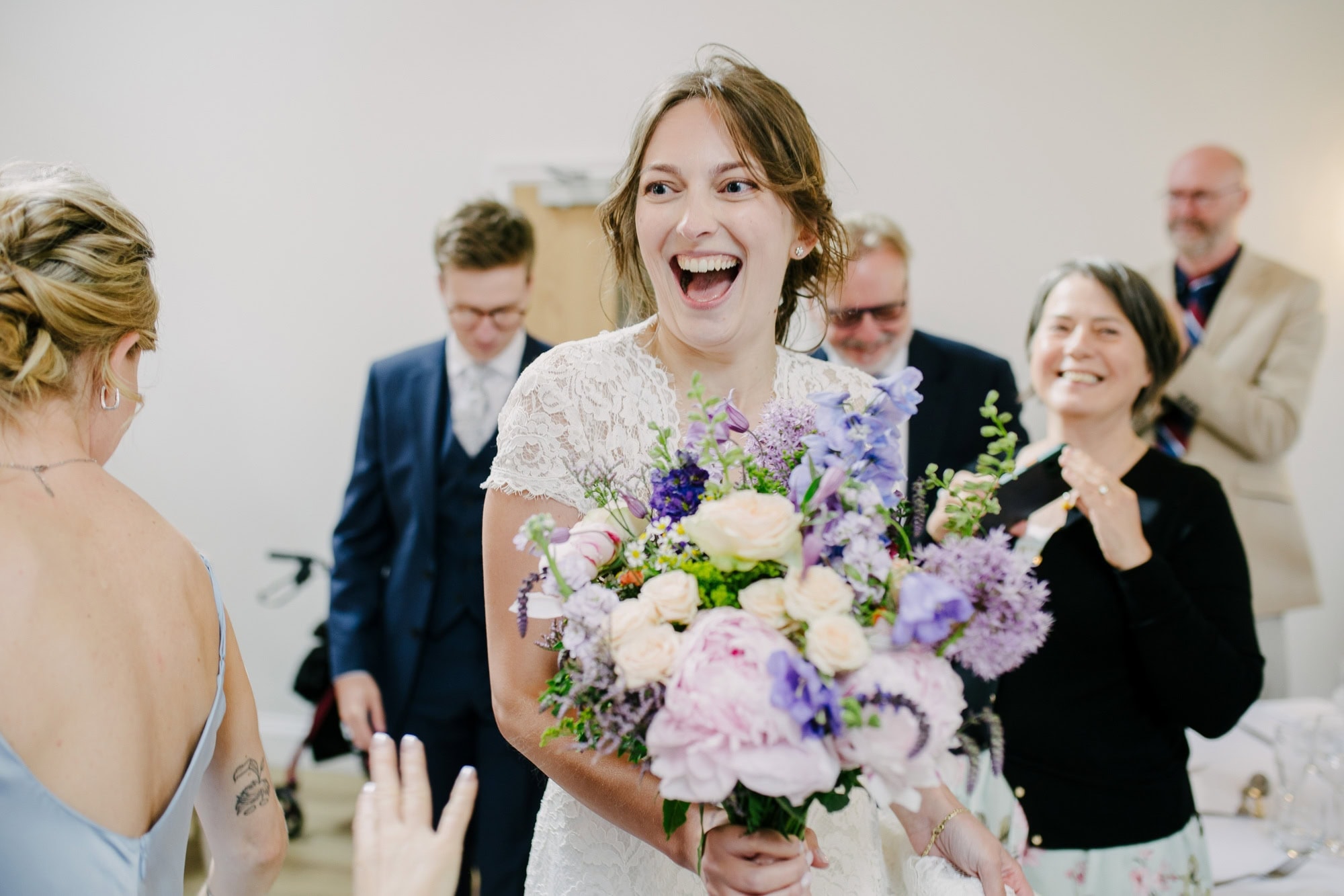 Ellie beaming with her bouquet as guests cheer the newlyweds into the wedding breakfast