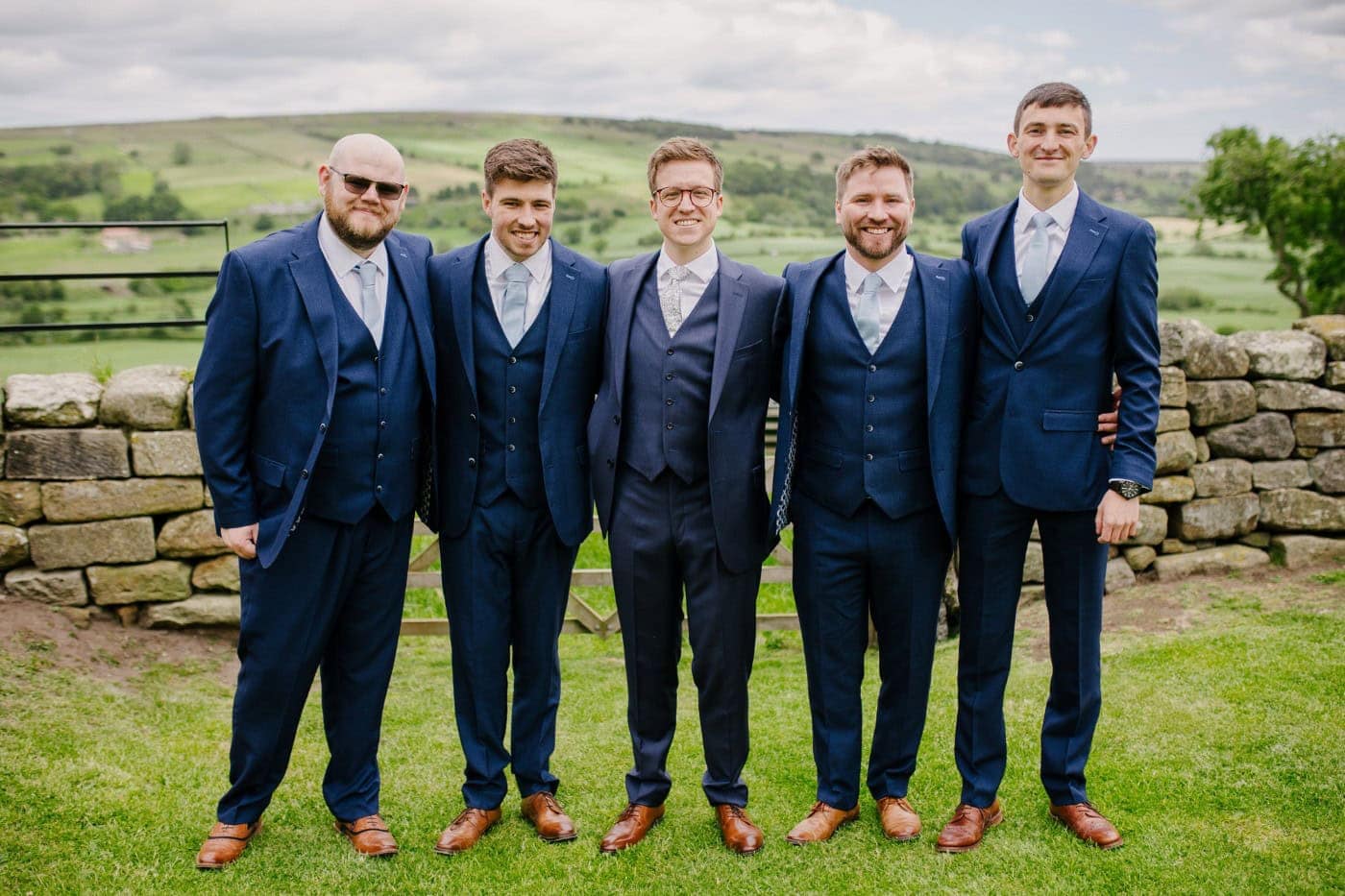 George and his groomsmen in navy suits on the hillside at Danby Castle
