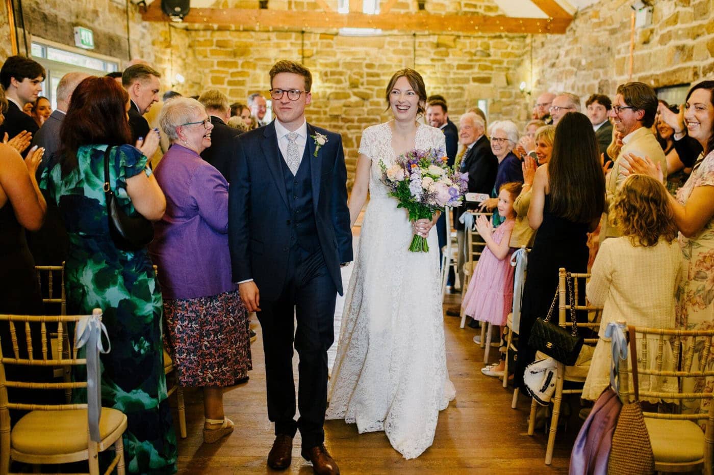 Ellie and George walking back up the aisle at Danby Castle to cheers as husband and wife