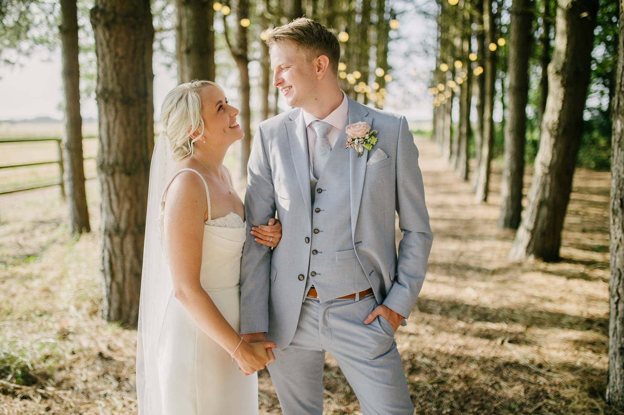 Bride and groom smiling at each other among the tall trees in the woods at Bunny Hill in East Yorkshire