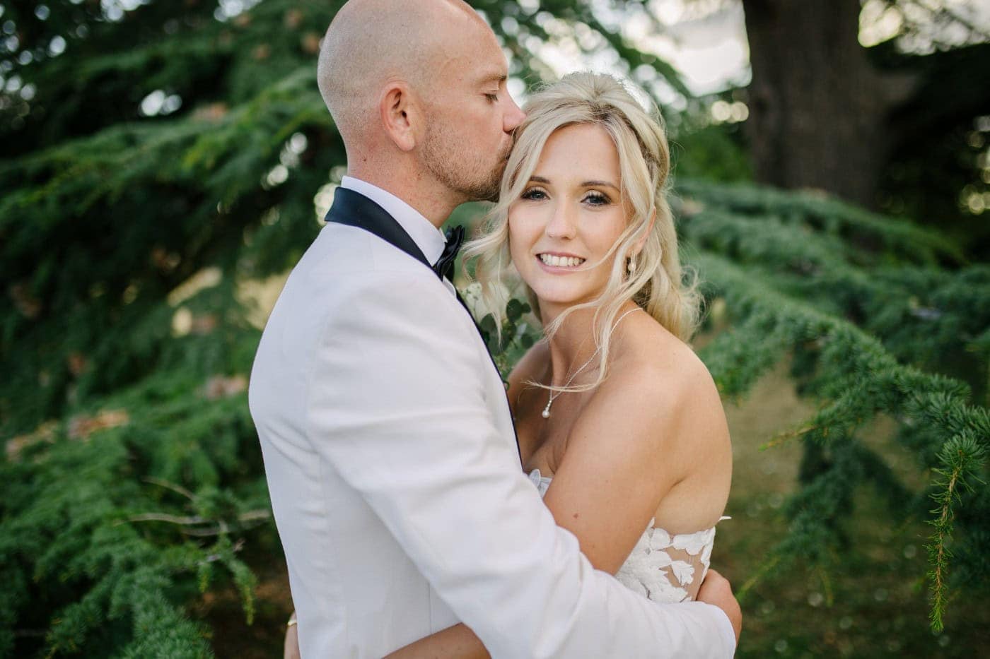 Groom kissing the bride under an old cedar tree in the parkland at Stubton Hall